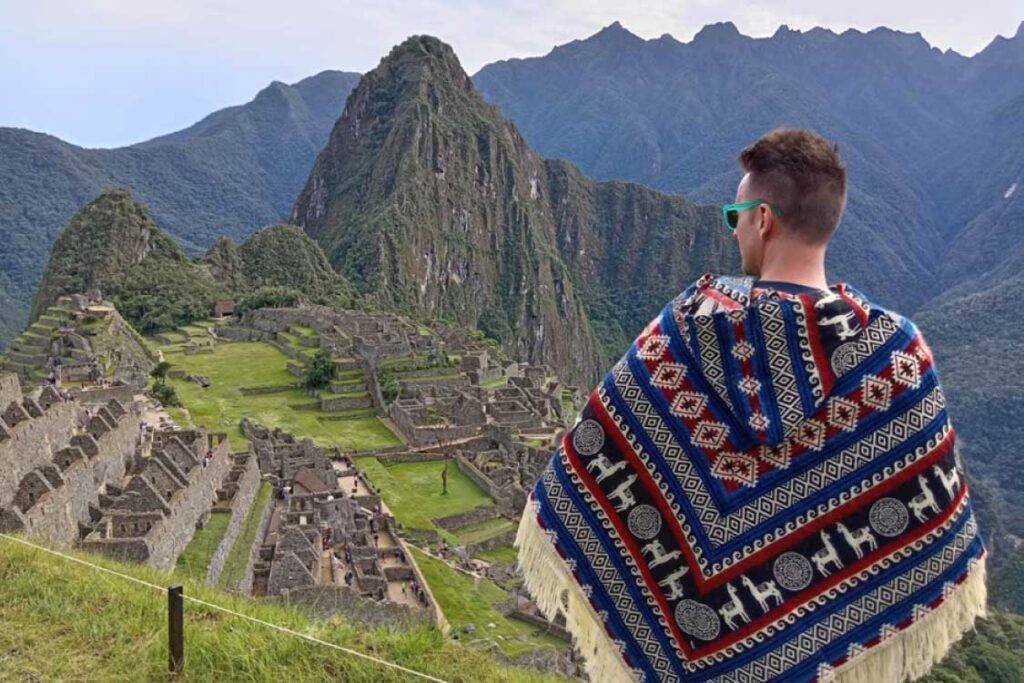 Traveler wearing traditional Andean poncho overlooking Machu Picchu, highlighting the cultural richness of Peru packages.
