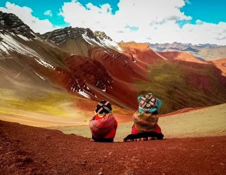 Two women in traditional clothing sitting at the top of Rainbow Mountain