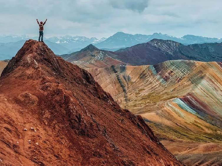 Palcoyo Mountain Tour, traveler celebrating at the top of the vibrant multi-colored mountain landscape in Peru