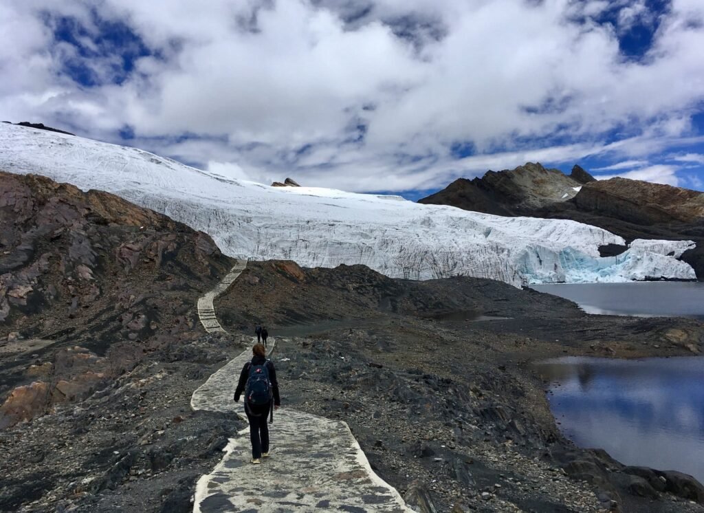 Pastoruri Glacier tour with visitor walking toward glacier under dramatic skies in the Andes